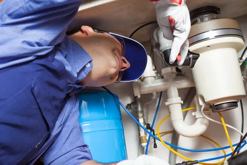Technician inspecting a garbage disposal beneath a kitchen sink