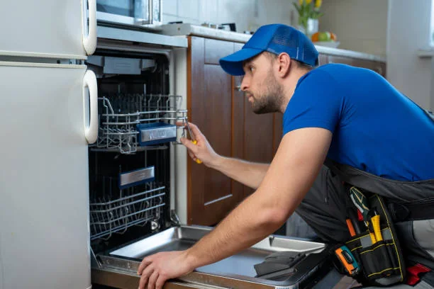 Technician inspecting appliance components beside a refrigerator