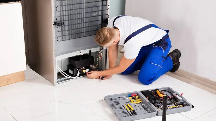 Technician checking refrigerator cooling components in a residential kitchen